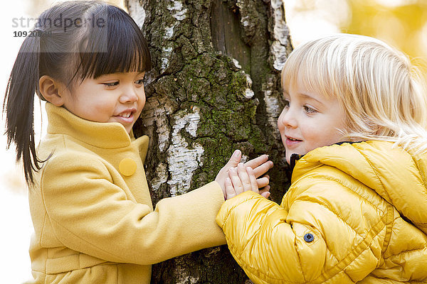 Vietnamesisches Mädchen und kaukasischer Junge spielen in der Herbstsaison im Wald.