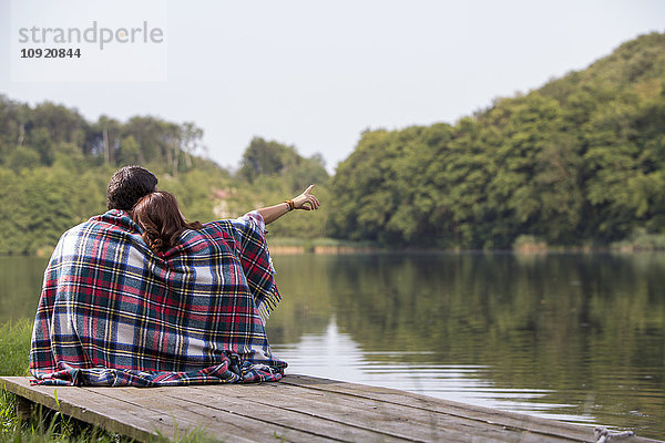 Rückansicht eines jungen Paares auf einem Steg am See