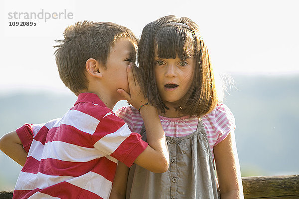 Kleiner Junge flüstert seiner Freundin ein Geheimnis ins Ohr.