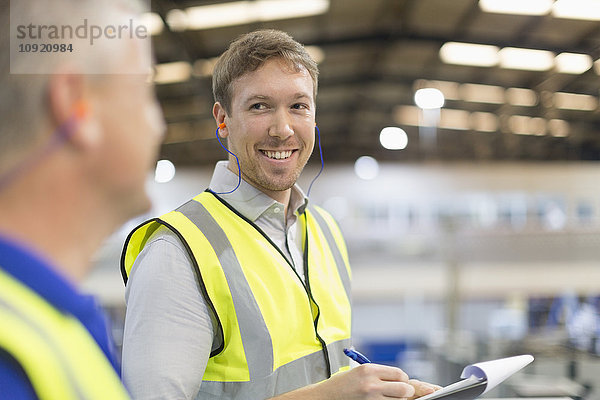 Supervisor mit Klemmbrett lächelndem Arbeiter in der Stahlfabrik
