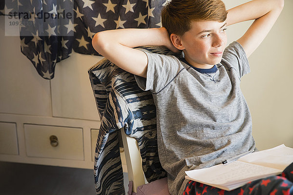 Selbstbewusster Junge macht Hausaufgaben mit den Händen hinter dem Kopf