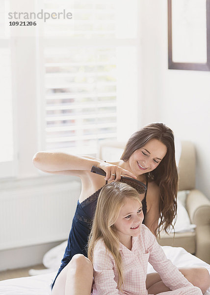 Mutter bürstet das Haar der Tochter auf dem Bett.