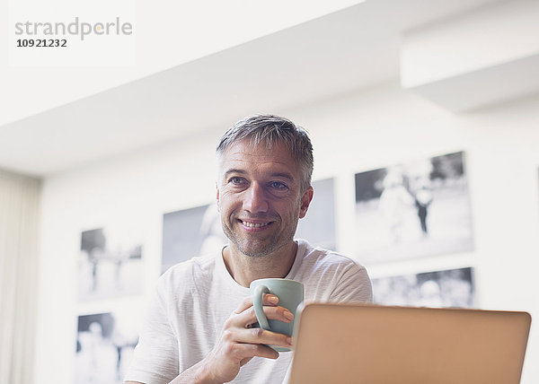 Lächelnder Mann trinkt Kaffee am Laptop