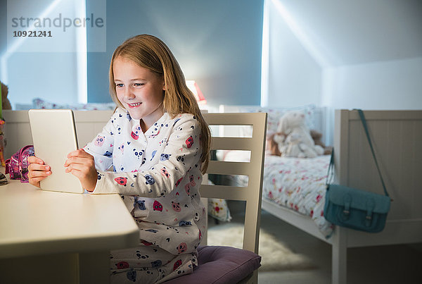 Mädchen im Pyjama mit digitalem Tablett am Schreibtisch im Schlafzimmer