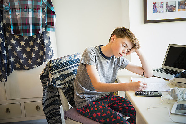 Gelangweilter Junge macht Mathe-Hausaufgaben am Schreibtisch im Schlafzimmer