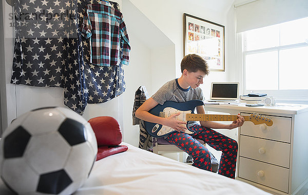 Junge spielt E-Gitarre im Schlafzimmer