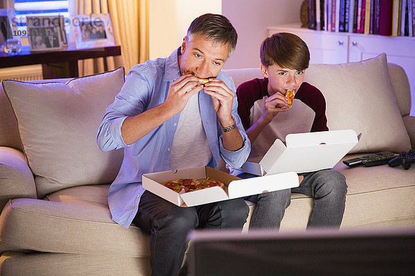 Vater und Sohn beim Pizzaessen und Fernsehen im Wohnzimmer