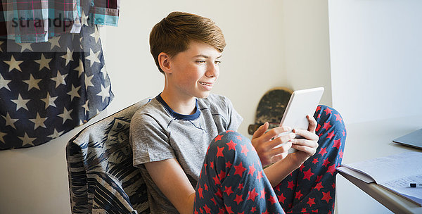 Junge im Schlafanzug mit digitalem Tablett im Schlafzimmer