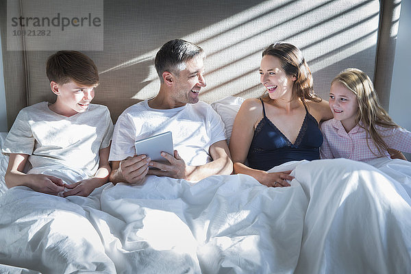 Lächelnde Familie im Bett liegend mit digitalem Tablett