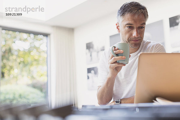 Mann trinkt Kaffee und arbeitet am Laptop in der Küche