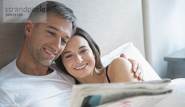 Lächelndes Paar liest Zeitung im Bett