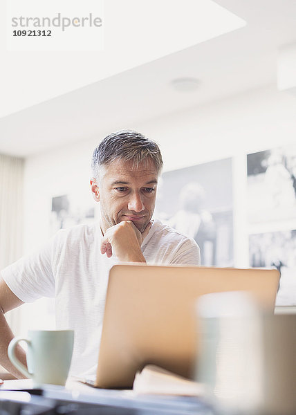 Mann trinkt Kaffee und arbeitet am Laptop in der Küche