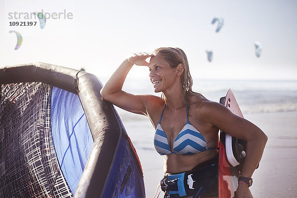 Lächelnde Frau mit Kiteboardausrüstung am Strand