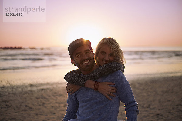 Porträt eines lächelnden Paares am Strand bei Sonnenuntergang