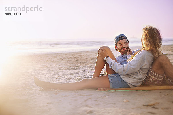 Lächelndes Paar  das sich am Strand bei Sonnenuntergang entspannt und unterhält.