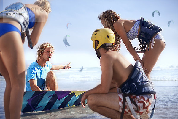 Mann unterrichtet Freunde beim Kitesurfen am sonnigen Strand