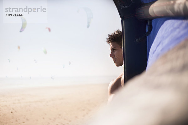 Nachdenklicher Mann  der hinter dem Kitekite am sonnigen Strand wegschaut