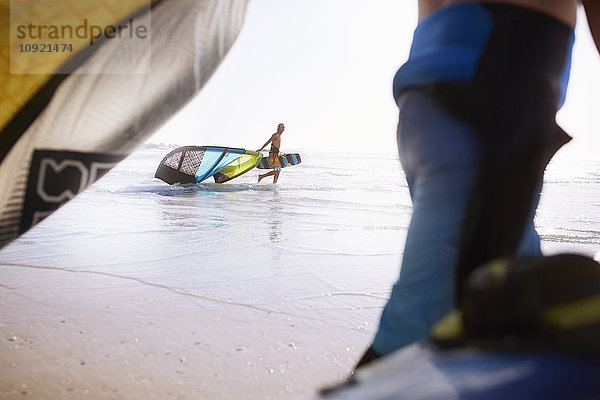 Mann  der Kiteboardausrüstung ins Meer zieht.