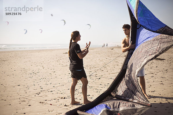 Frau unterrichtet Mann mit Kitesurfdrachen am sonnigen Strand