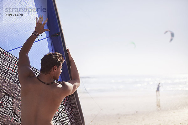 Mann hebt Drachen an sonnigen Strand