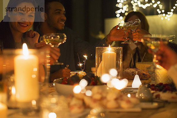 Freunde toasten Champagnergläser bei Kerzenschein am Weihnachtstisch