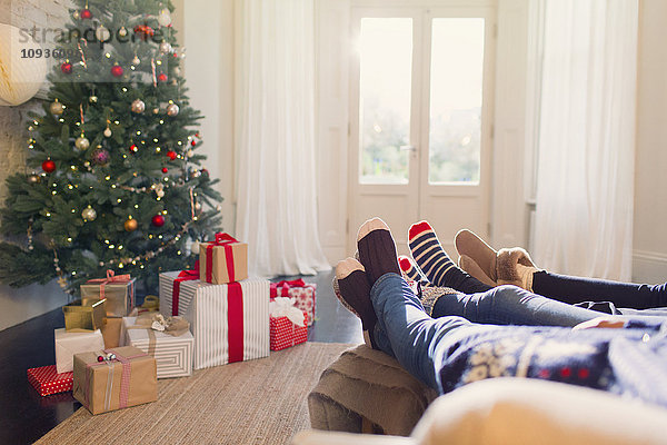 Entspannte Familie in Socken mit Füßen in der Nähe des Weihnachtsbaums