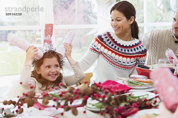 Verspieltes Mädchen mit Weihnachtsgebäck auf dem Kopf am Tisch