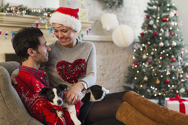 Liebespaar mit Hund entspannt im Wohnzimmer mit Weihnachtsbaum