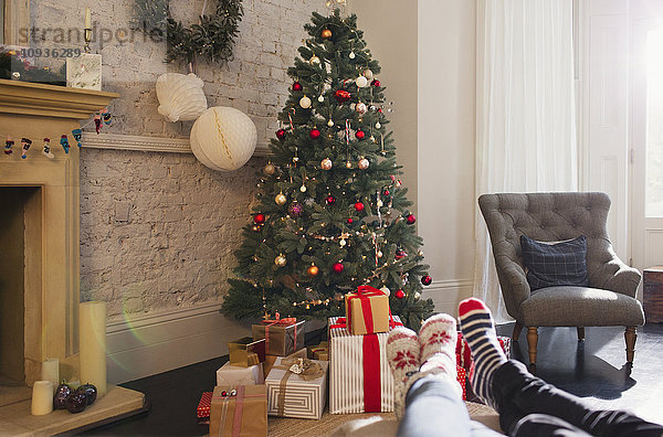 Entspanntes Paar mit Socken und Füßen in der Nähe des Weihnachtsbaums im Wohnzimmer