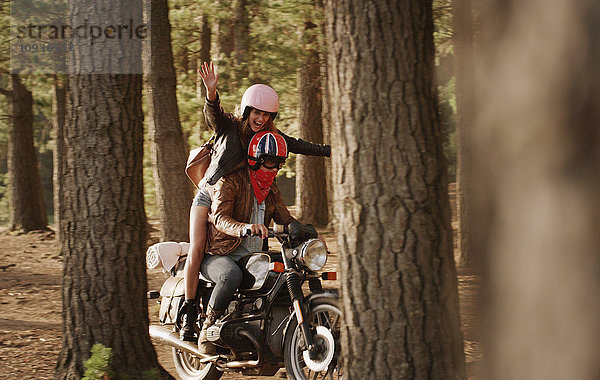 Übermütige junge Frau beim Motorradfahren im Wald