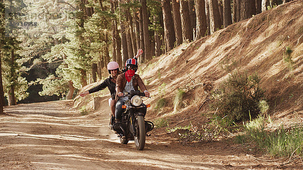 Übermütige junge Frau fährt Motorrad auf unbefestigtem Weg im Wald