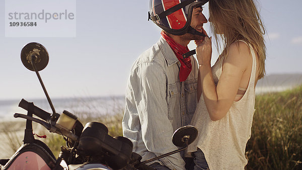 Verliebtes junges Paar auf einem Motorrad mit Strand im Hintergrund