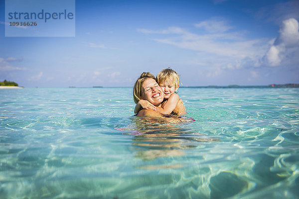 Begeisterte Mutter  die ihren Sohn im tropischen Ozean umarmt