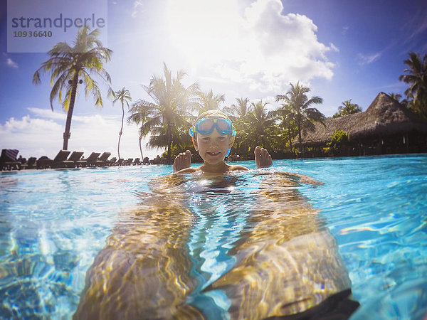 Portrait lächelnder Junge im sonnigen tropischen Schwimmbad