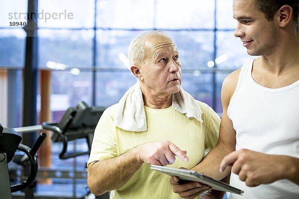 Fitnesstrainer zeigt Tablette an älteren Mann