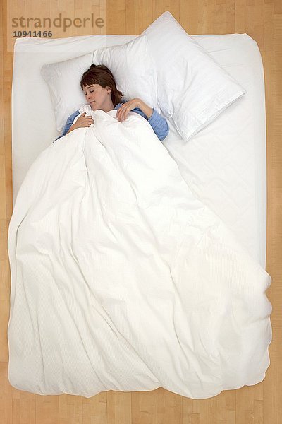 Frau liegt im Bett und hält die Bettdecke