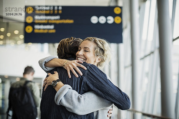 Glückliche Geschäftsfrau umarmt männlichen Kollegen am Flughafen