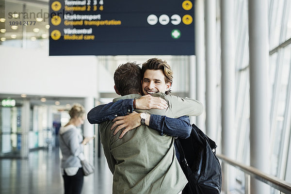 Glücklicher Geschäftsmann umarmt männlichen Kollegen am Flughafen