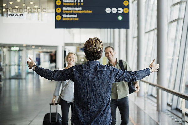 Rückansicht des Geschäftsmannes mit ausgestreckten Armen bei der Begrüßung der Kollegen am Flughafen