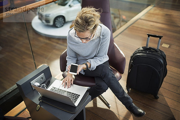 Hochwinkelansicht der Geschäftsfrau mit Laptop und Smartphone in der Flughafenlobby
