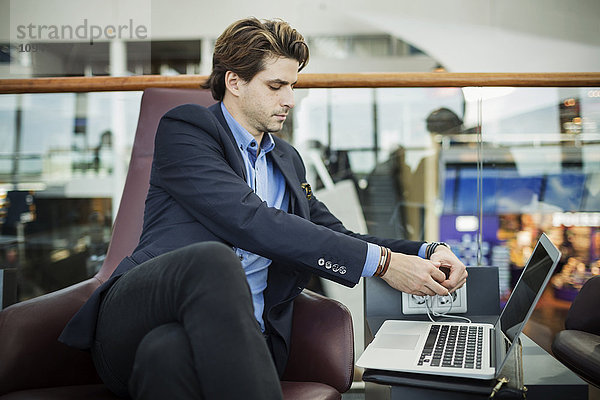 Geschäftsmann verbindet Stecker mit Laptop in der Flughafen-Lobby