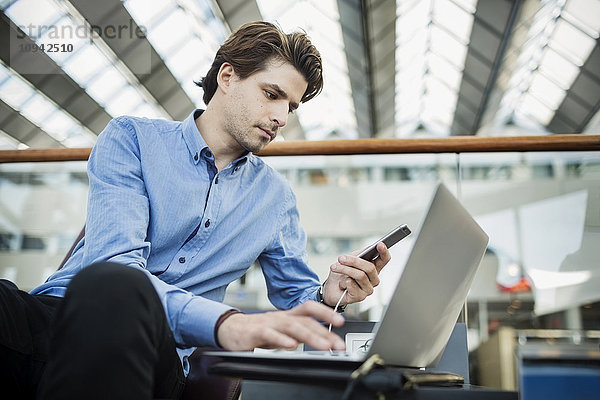 Geschäftsmann mit Laptop und Smartphone in der Flughafenlobby