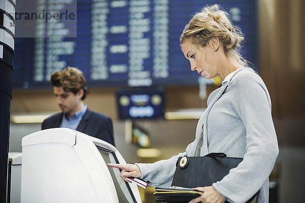 Seitenansicht der Geschäftsfrau mit Check-in-Maschine am Flughafen