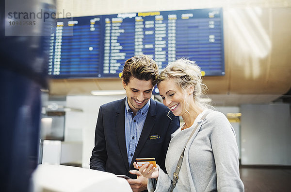 Glückliche Geschäftsleute  die am Flughafen auf Kreditkarte schauen