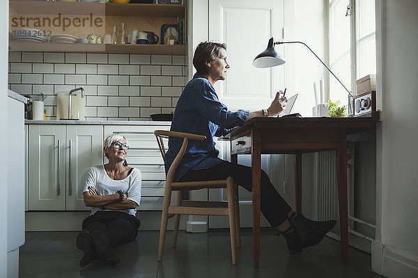 Industrie-Designerin schaut Kollegin an  während sie in der Küche auf dem Boden sitzt.