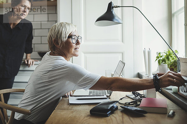 Industriedesigner beim Einstellen des Radios  während der Kollege im Hintergrund im Home Office steht.