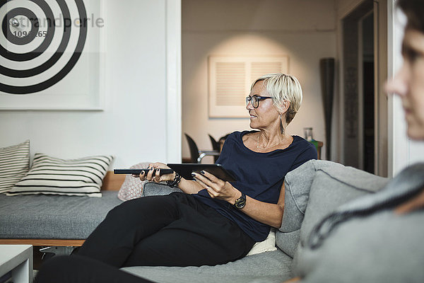 Industriedesigner mit Fernbedienung beim Sitzen mit Kollegen auf dem Sofa zu Hause