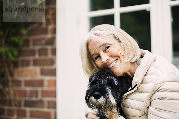 Porträt einer glücklichen Seniorin mit Hund vor dem Haus