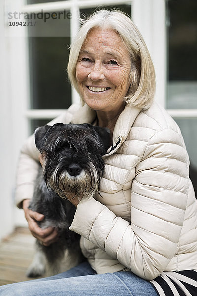 Porträt einer lächelnden Seniorin  die mit Hund vor dem Haus sitzt