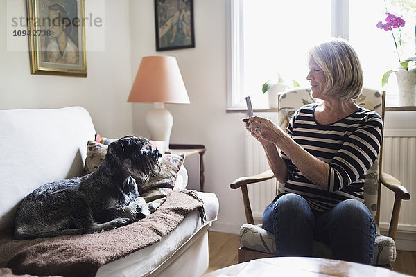 Senior Frau fotografiert Hund durch Smartphone zu Hause
